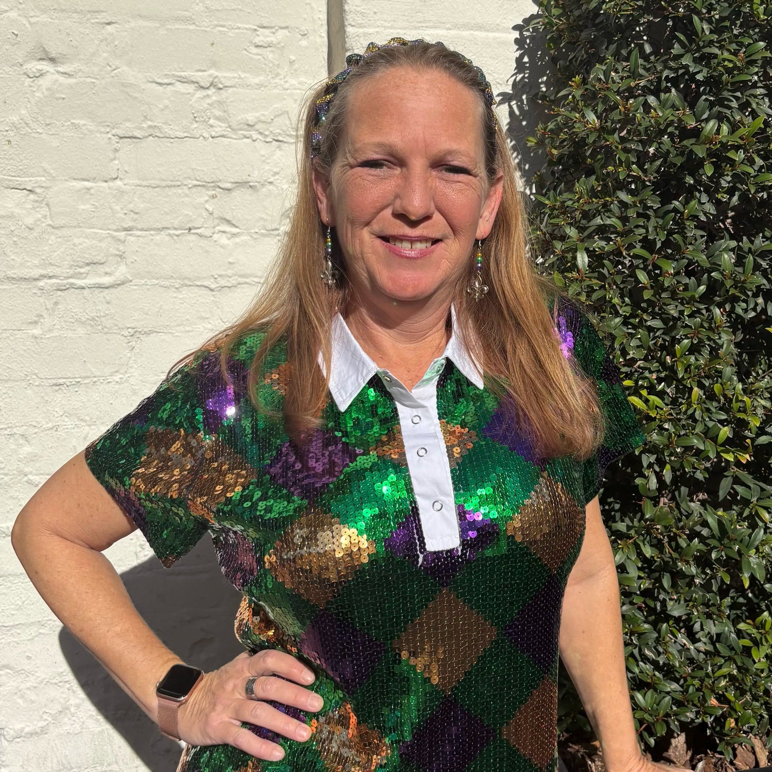 Woman wearing a sequined dress with Mardi Gras colors against a white wall.